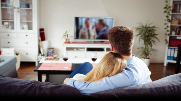 Feature | Back view of young couple enjoying themselves and watching tv on the sofa | Best Amazon TV Shows You Need to Watch ASAP