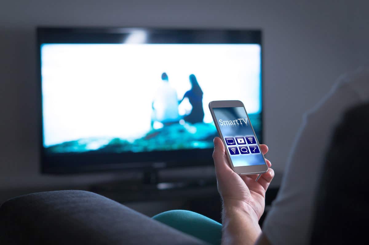 Man watching television and using smart tv remote control application on mobile phone | Don't Dump Your Old Phone: 15 Things You Can Do With Your Old Smartphone