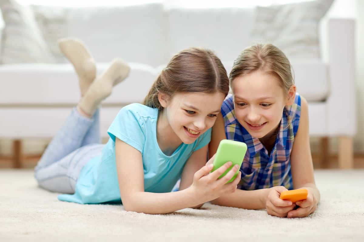  Two girls lying on the floor and using smartphones for educational purposes.