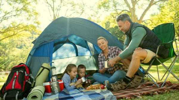 Feature | Family having snacks and coffee outside the tent at campsite | Cool Camping Must-Haves To Survive A Weekend Outdoors