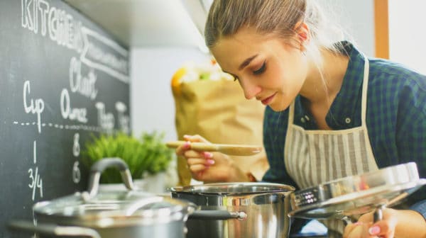 Feature | Young woman cooking in her kitchen standing near stove | Smart Kitchen Decor And Gadgets That Will Make Cooking More Fun