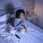 Woman eating popcorn on bed watching movie