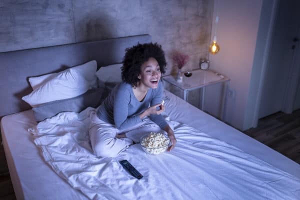 Woman eating popcorn on bed watching movie